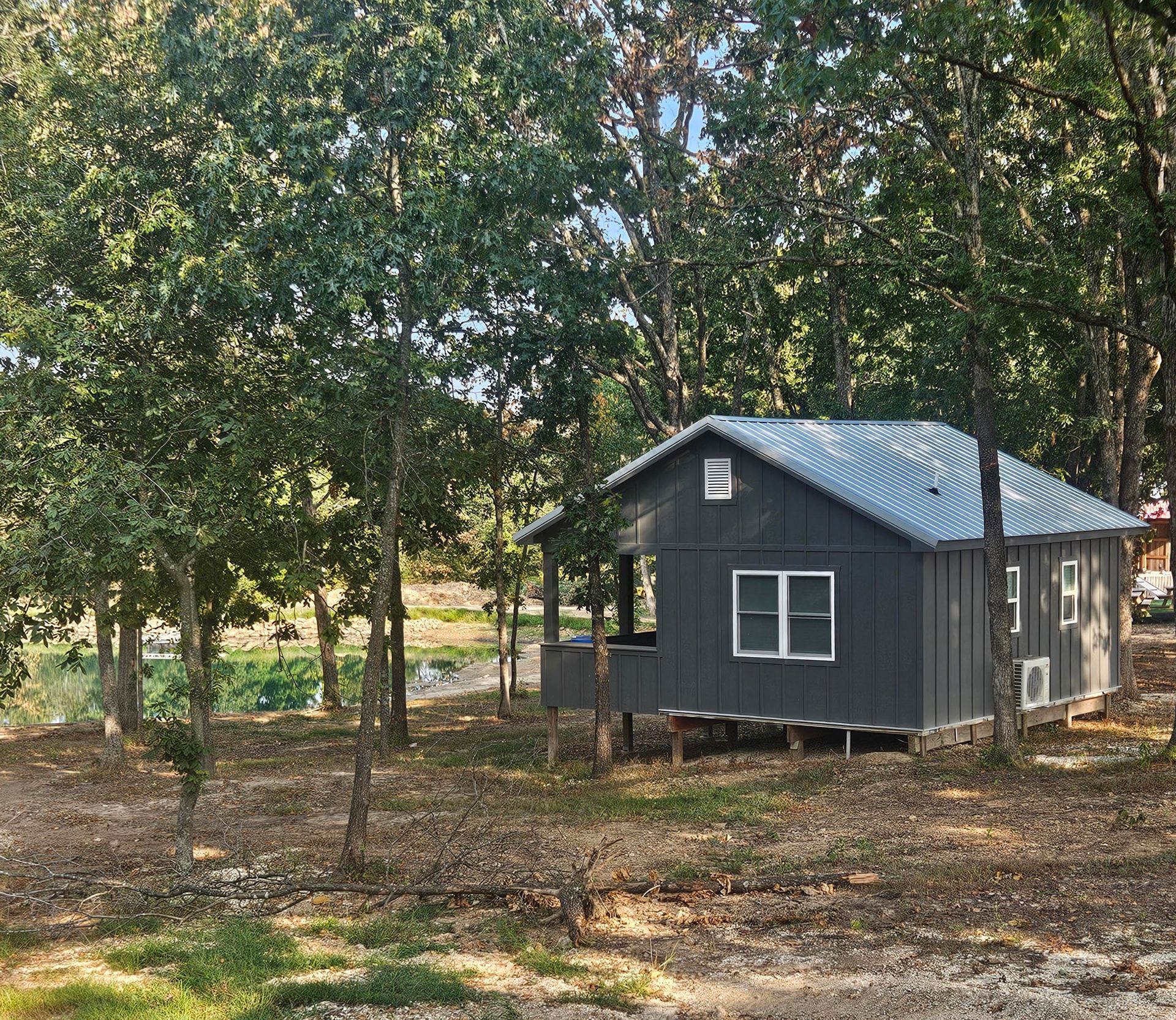 Small dark cabin with a metal roof among trees in a wooded area