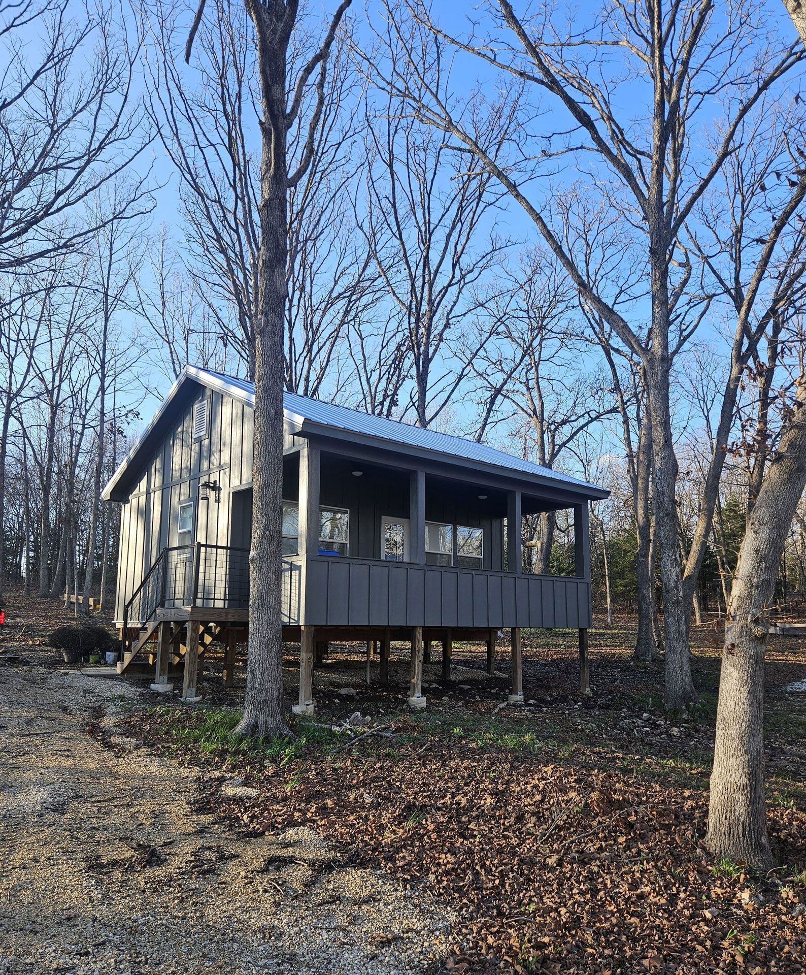 Small cabin porch in a wooded area, with bare trees and a leaf-covered ground.