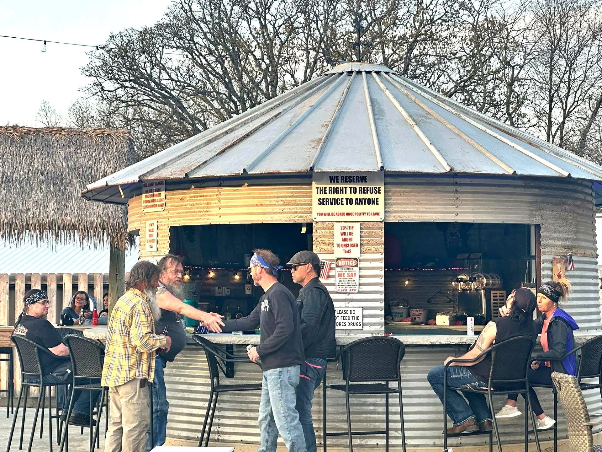 People chatting at an outdoor bar kiosk with a metal roof and stools on a winter day