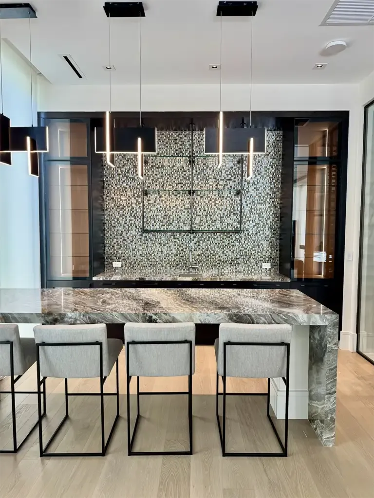 Contemporary home bar with mosaic tile backsplash, marble waterfall counter, and floating glass shelves by Kitchen & Bath Studios Coconut Creek FL.