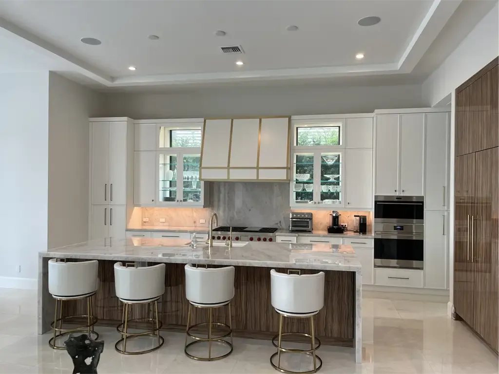 White and wood kitchen with gold hood accents by Kitchen & Bath Studios Inc.
