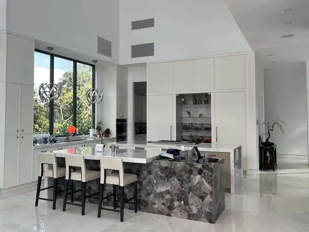 High ceiling kitchen with dark stone island by Kitchen & Bath Studios Inc.