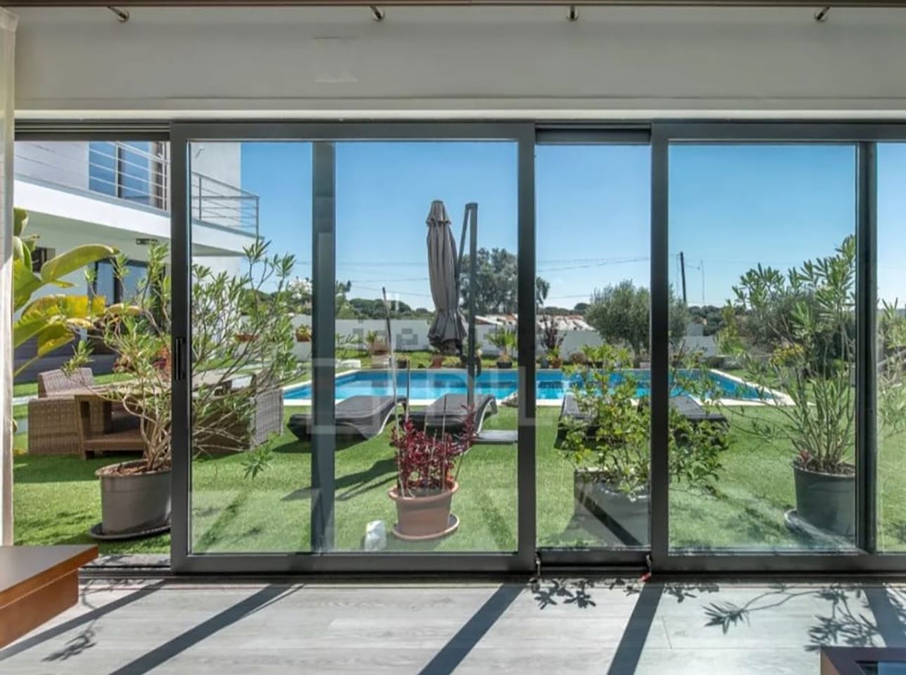 Portas de vidro deslizantes dão acesso a um pátio iluminado e a uma piscina no quintal, cercada por vegetação exuberante.
