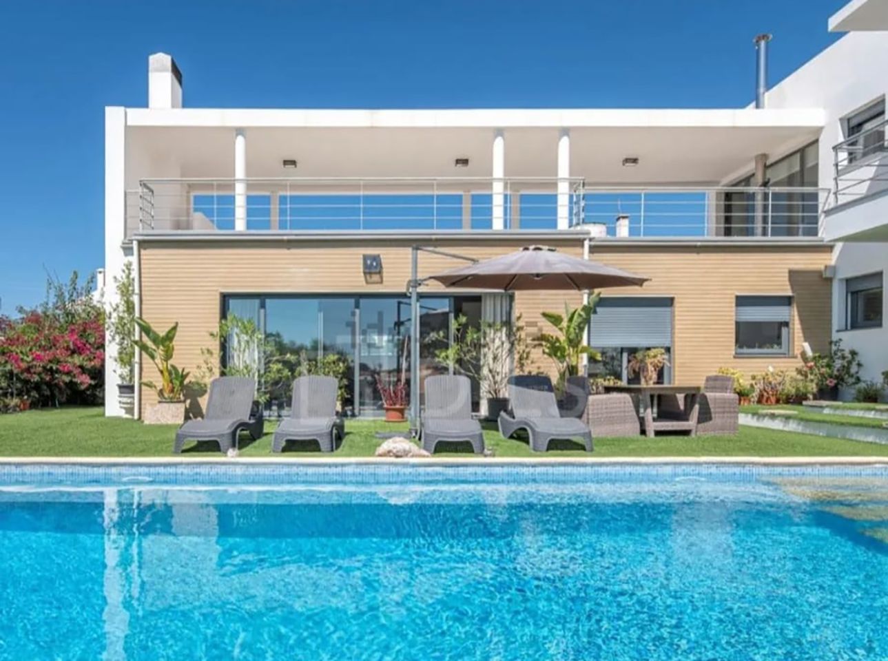 Casa moderna com área de estar no pátio ao lado de uma piscina azul sob um céu claro.