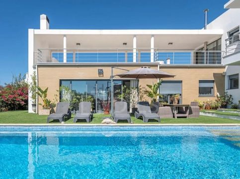 Casa moderna com área de estar no pátio ao lado de uma piscina azul sob um céu claro.
