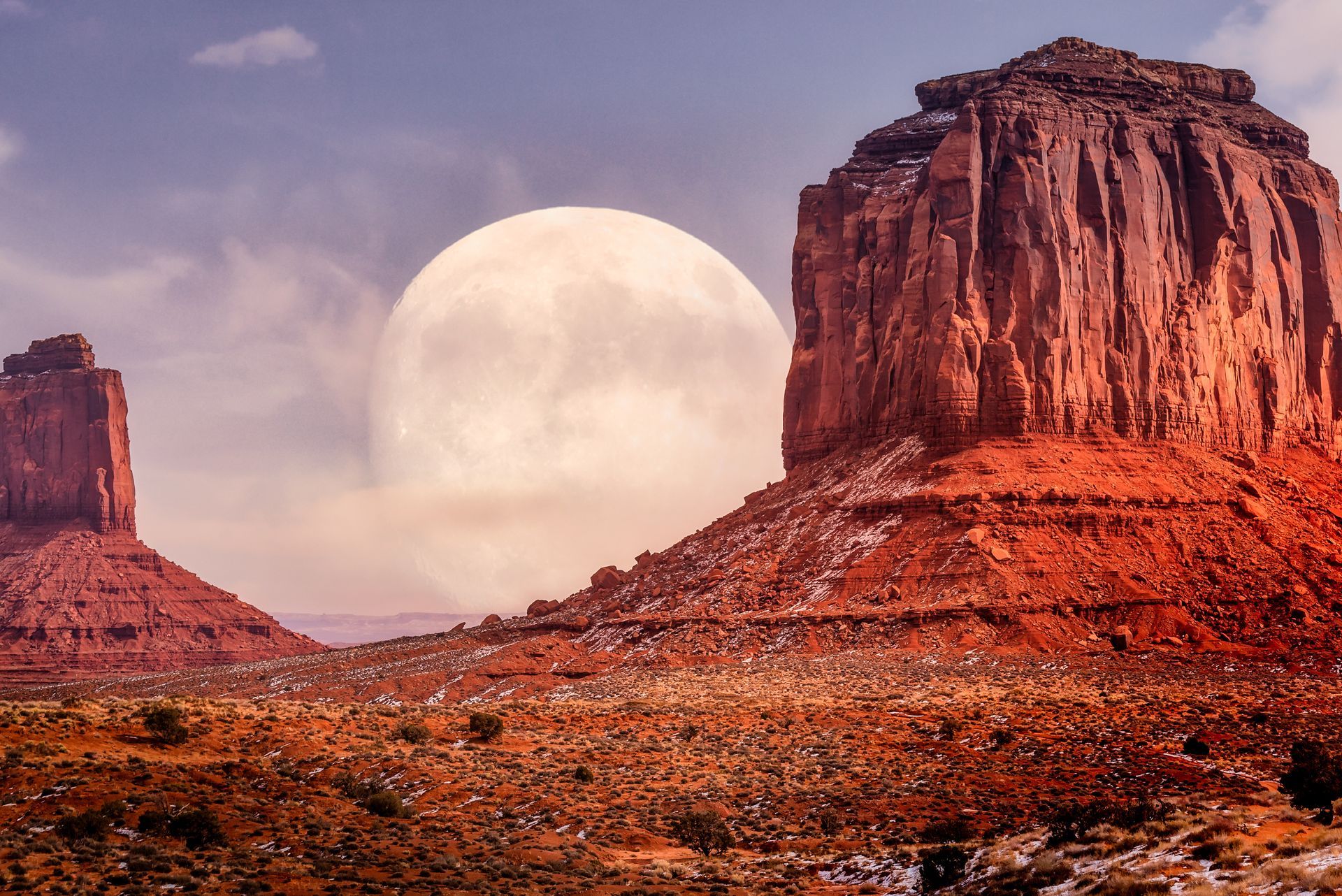Red desert mesas under a large full moon in a pink dusk sky