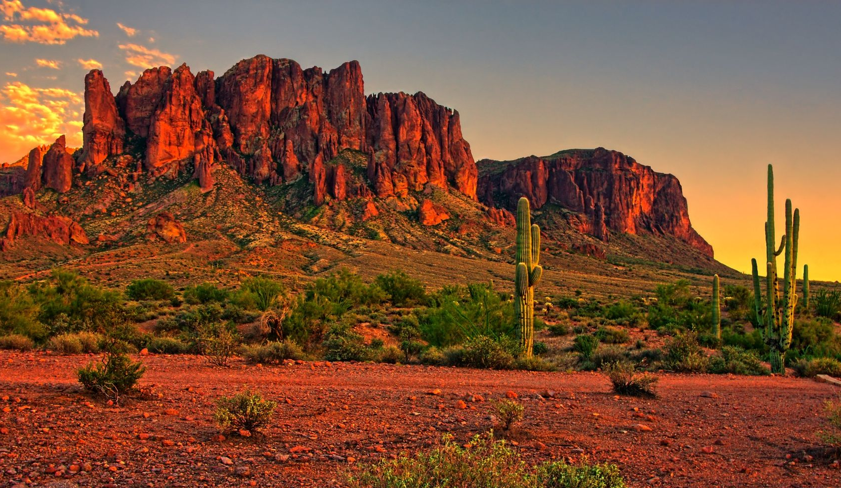 Sunlit red sandstone buttes and desert cacti at dusk in a rocky desert landscape