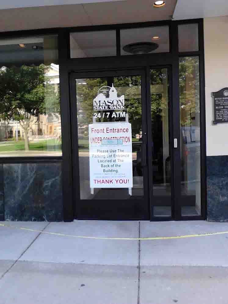 Exterior of a building with a glass door, sign indicating free entrance. Yellow tape across the sidewalk.