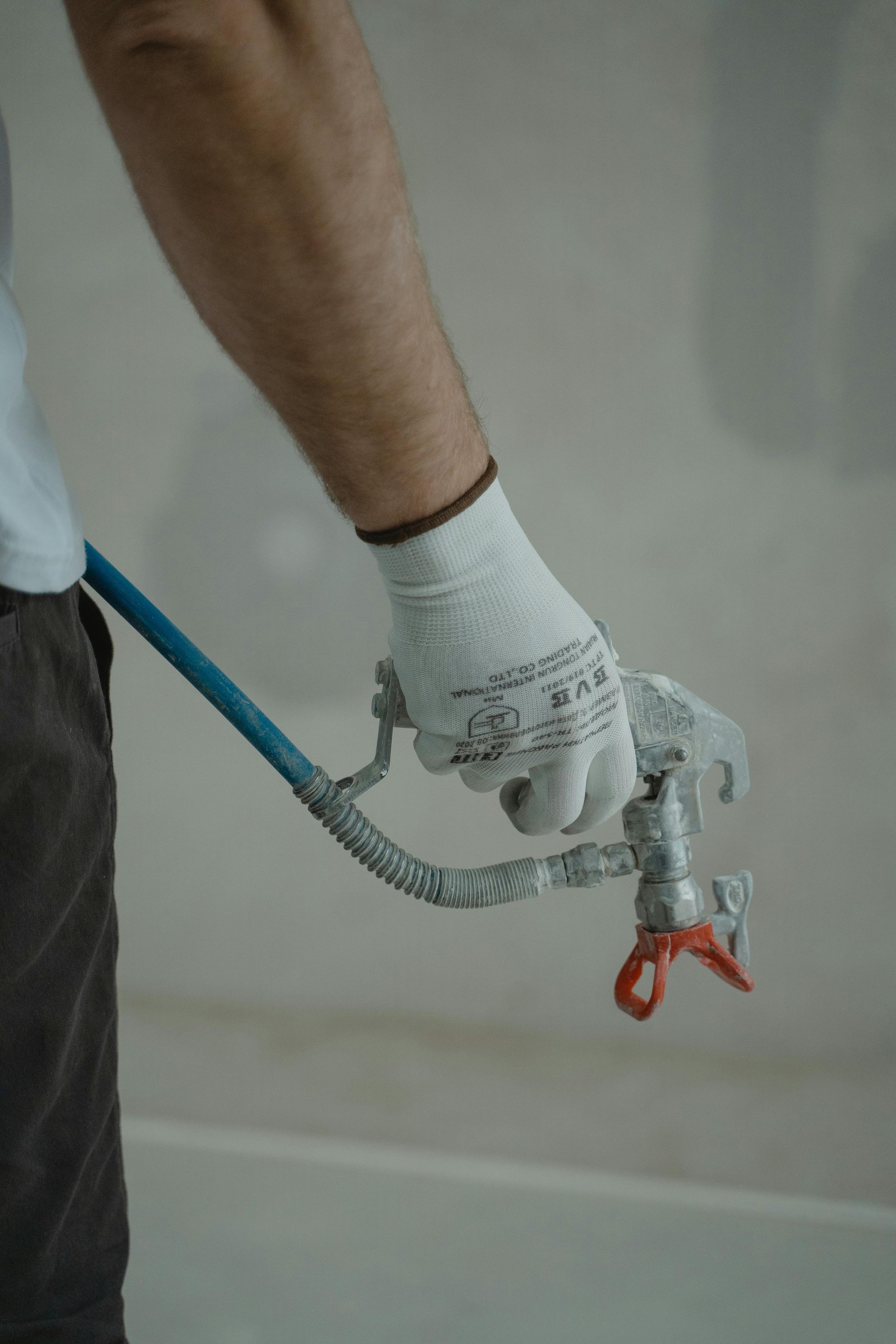 Person wearing work gloves holding a paint sprayer nozzle, indoors.