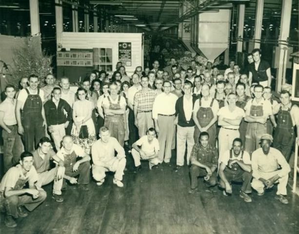 Large group posing in an industrial warehouse, with people standing and kneeling on a wooden floor.