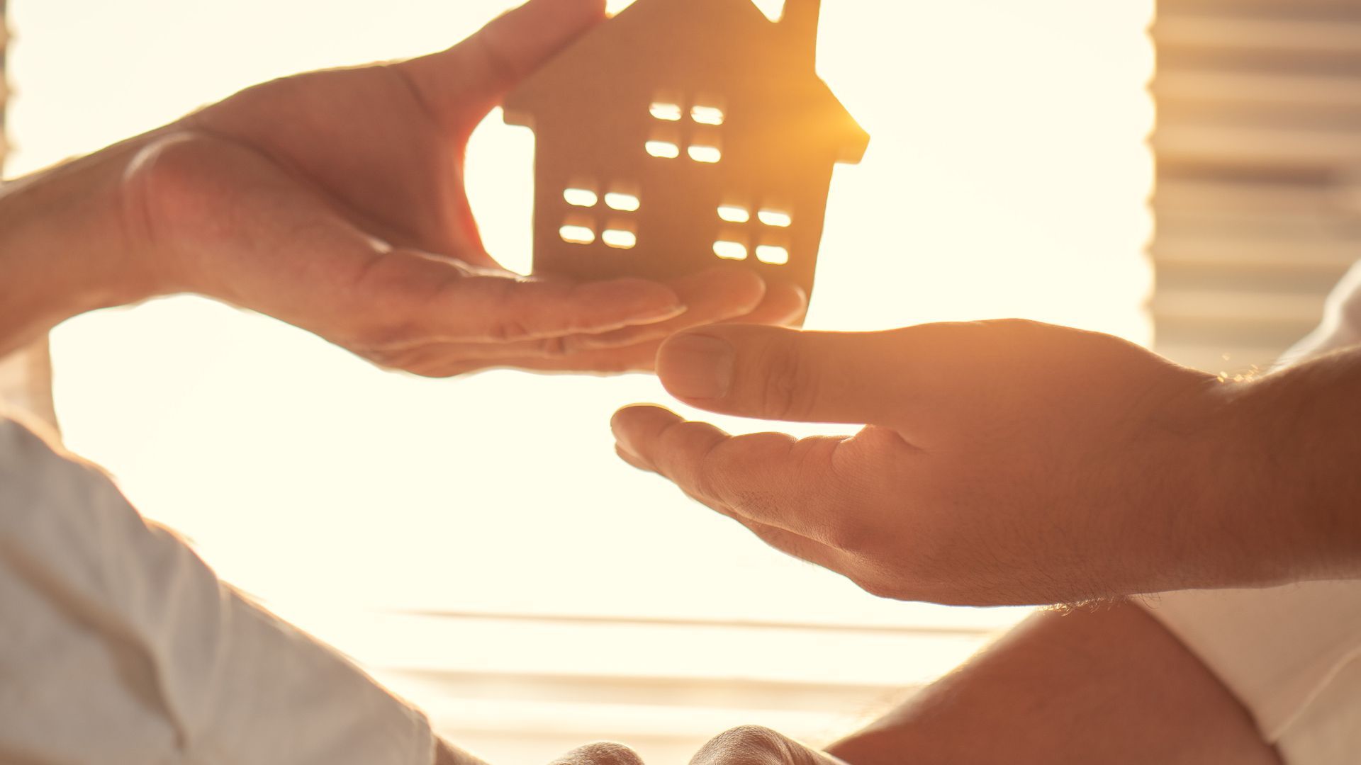 Hands passing a small house cutout under bright sunlight.