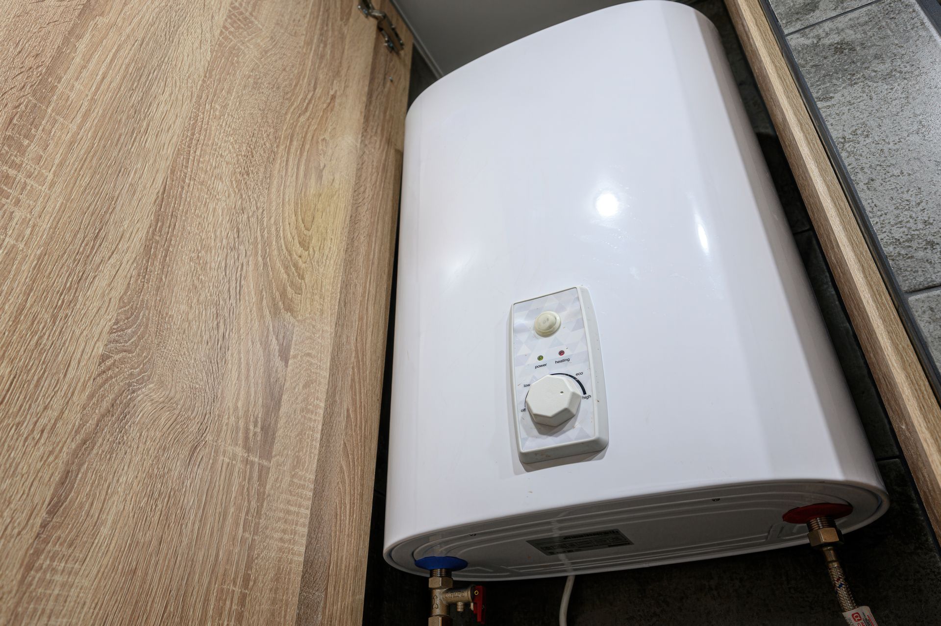 White wall-mounted water heater with control knob in a narrow utility space