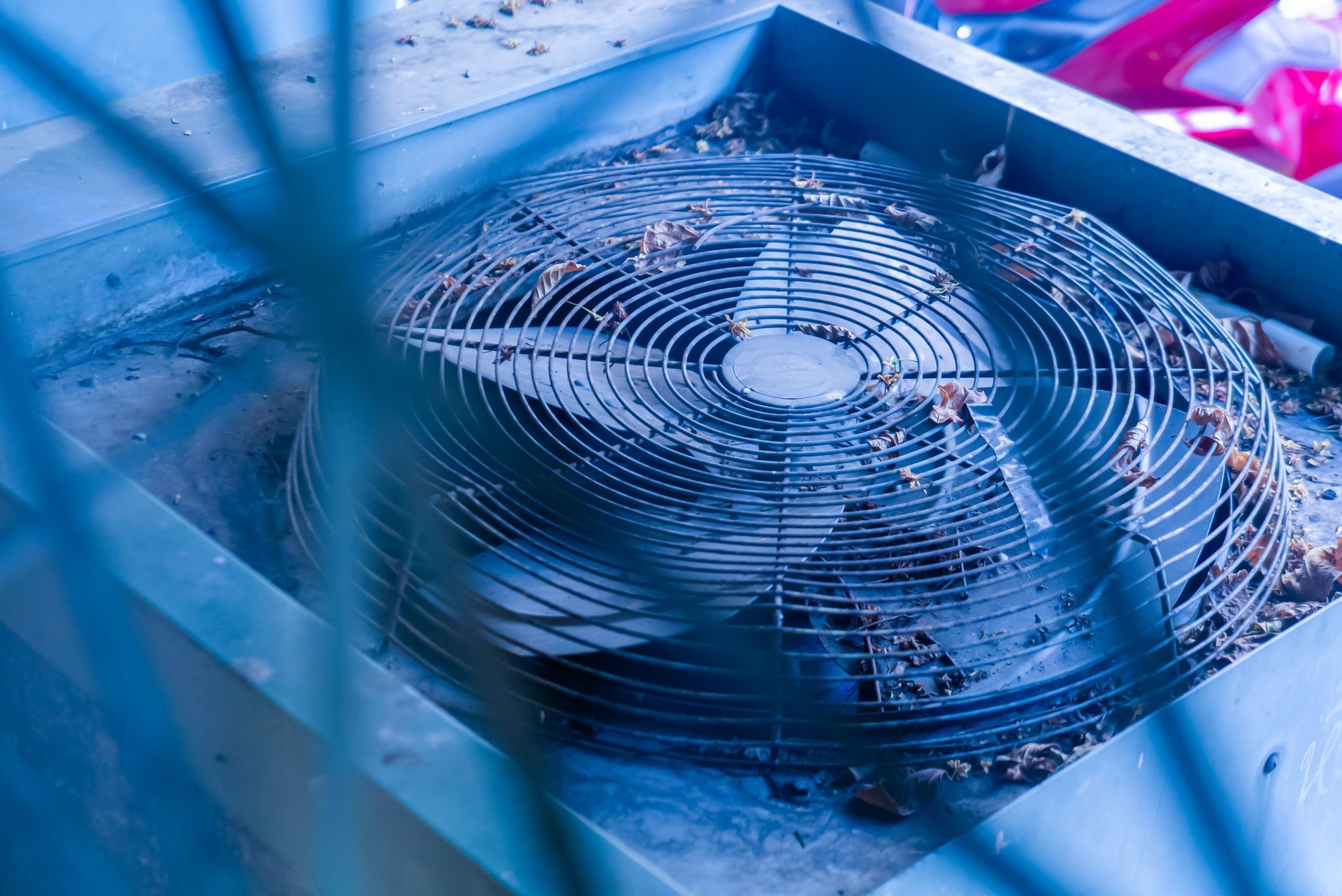 Blue industrial fan with protective grille on machinery, viewed through metal bars
