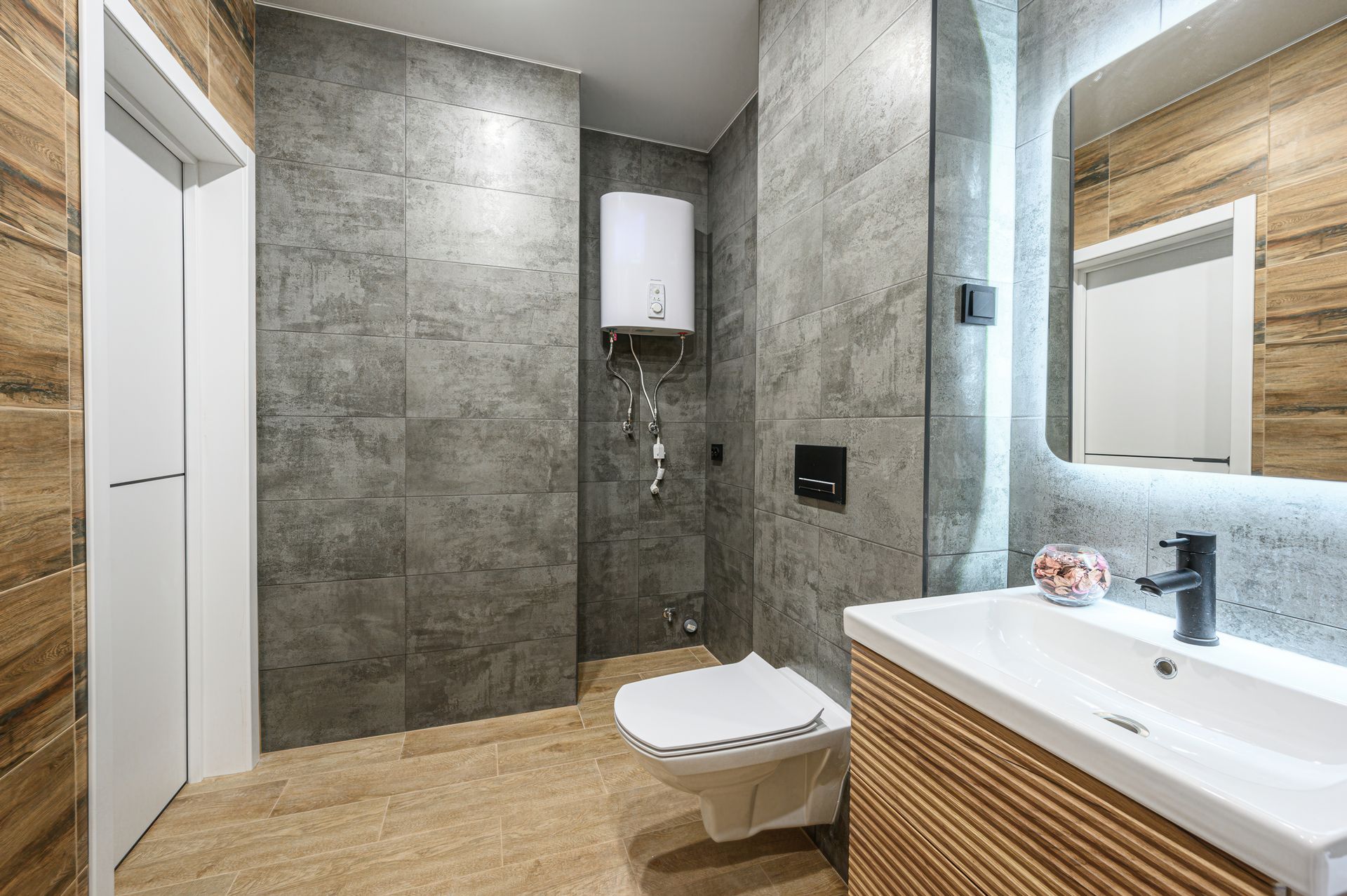 Modern bathroom with gray stone walls, wood vanity, white sink, and a wall-mounted toilet.