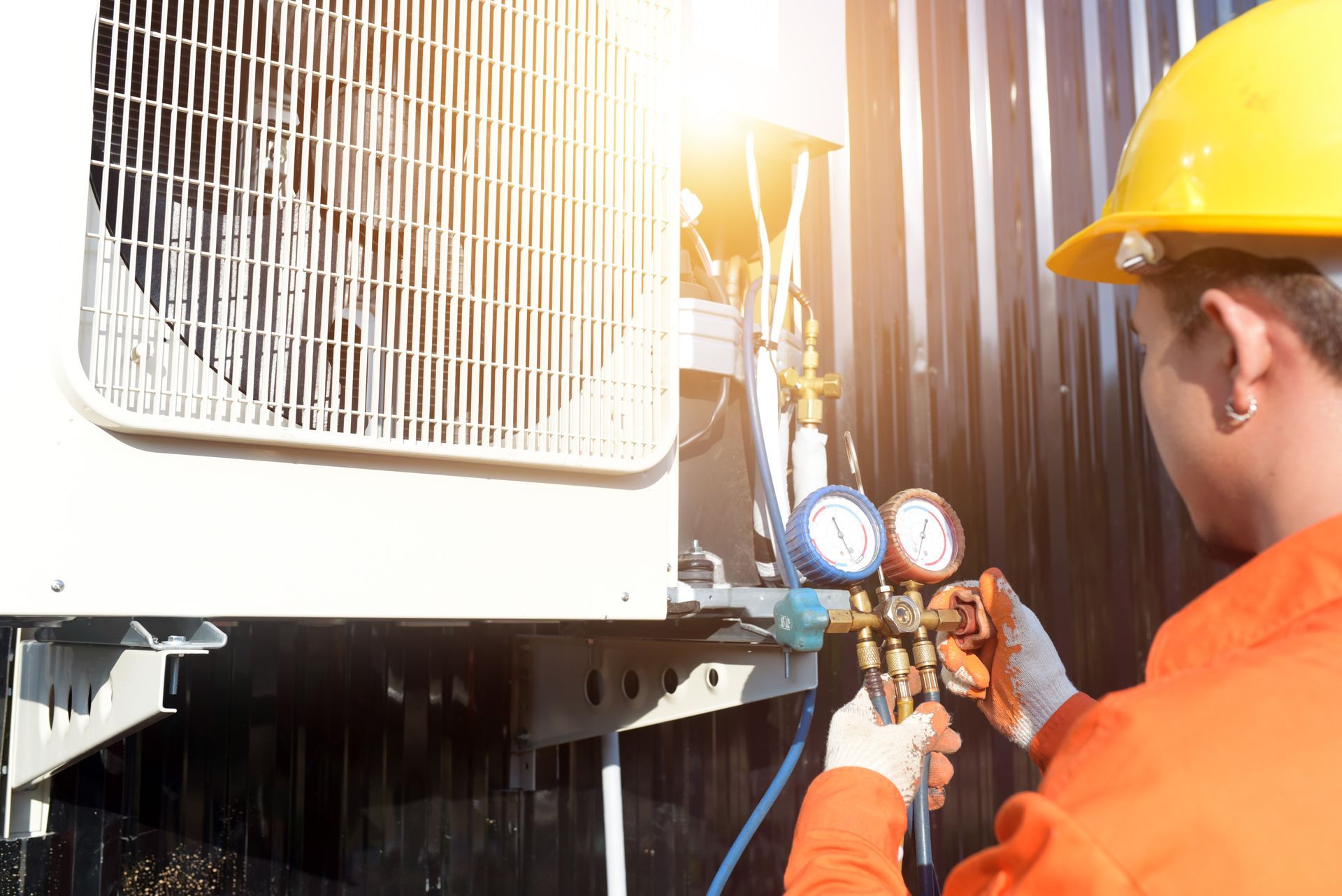 Worker in orange jacket and yellow hard hat adjusting gauges on industrial HVAC equipment