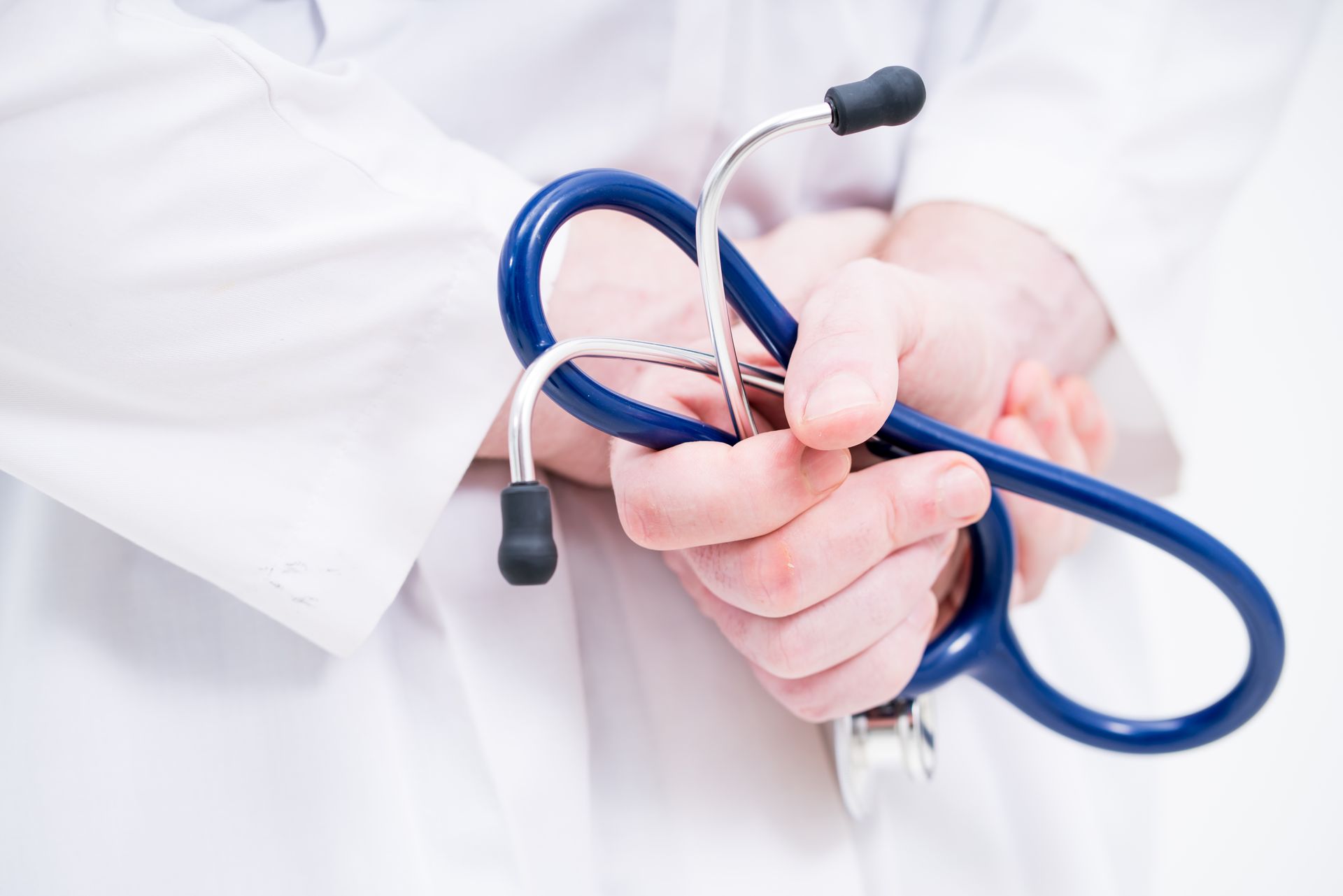 A medical professional in a white coat holds a blue stethoscope in their hands.
