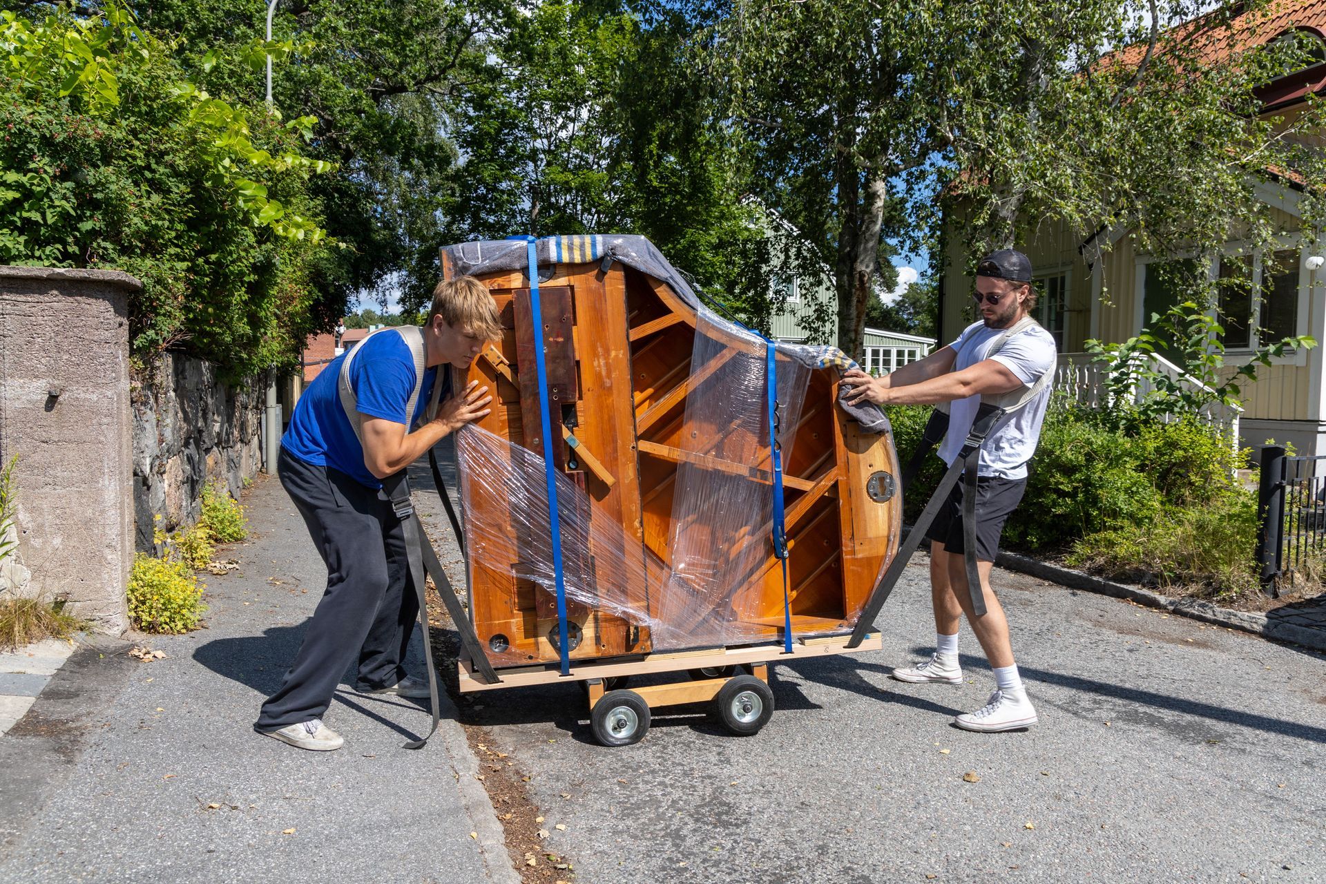 Professional Piano Movers securing a wrapped upright piano on a wheeled dolly for safe transport.