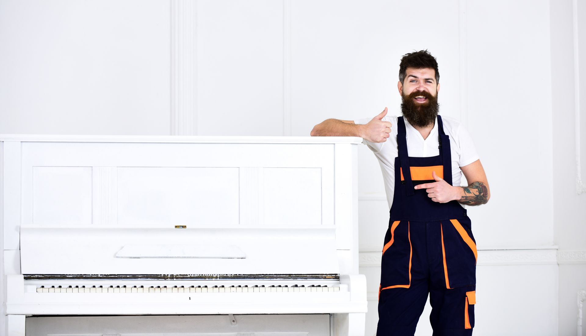 Person in work overalls giving thumbs up beside an upright piano.