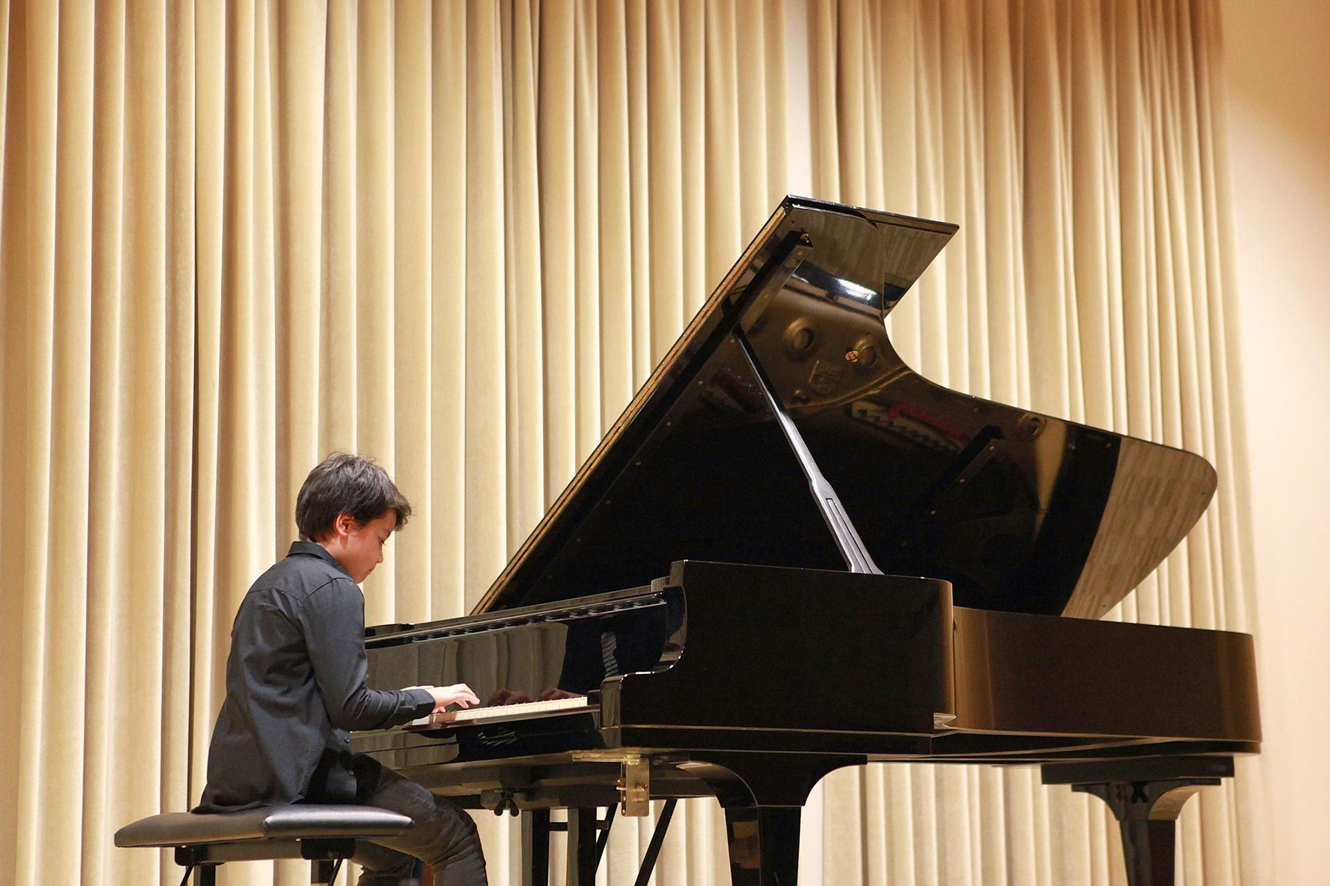 A man is playing a grand piano in front of a curtain.