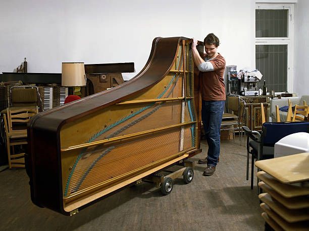 A man in a brown t-shirt and blue jeans moves a wooden piano, representing grand piano movers.