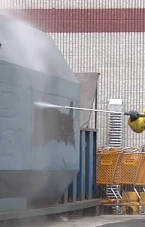 Worker using pressure washer to clean storefront area.