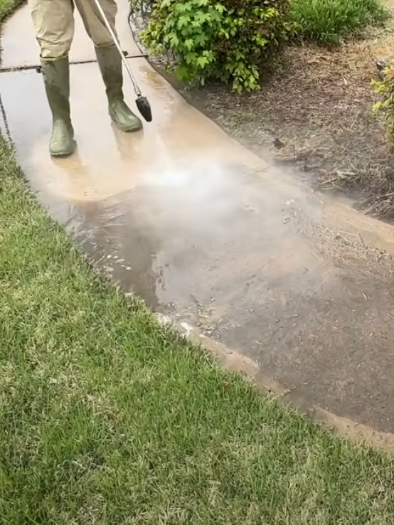 A person is using a pressure washer to clean a sidewalk.