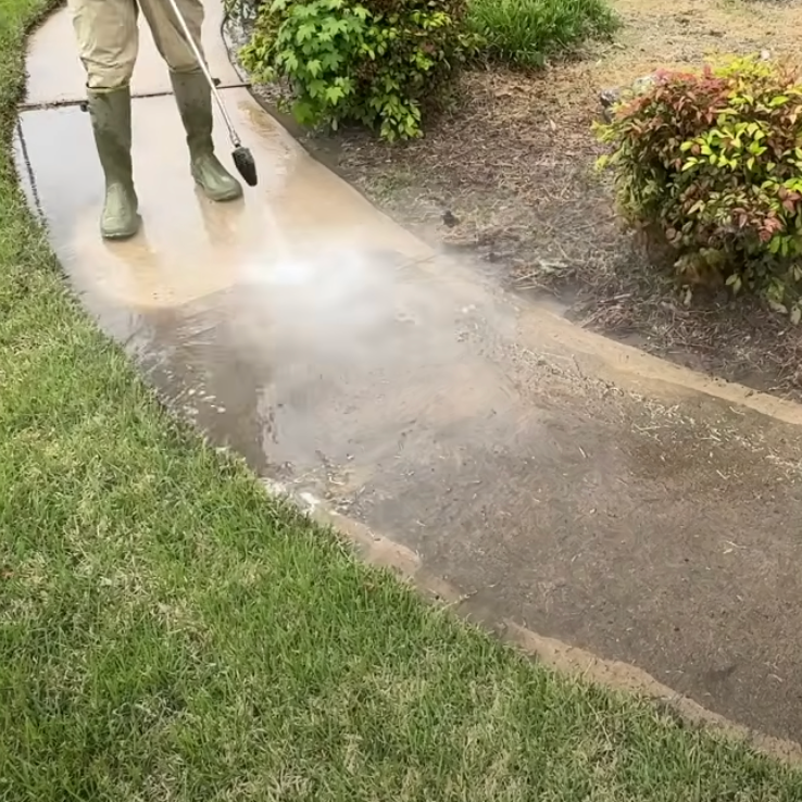 A person is using a pressure washer to clean a house driveway.