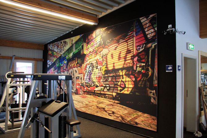 Ein Fitnessstudio mit einem großen Wandbild an der Wand