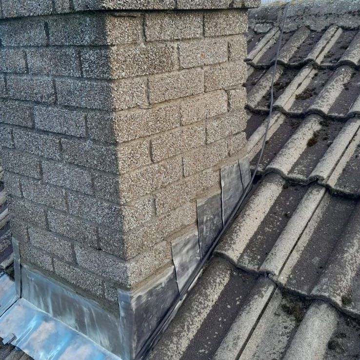 A brick chimney is sitting on top of a tiled roof.
