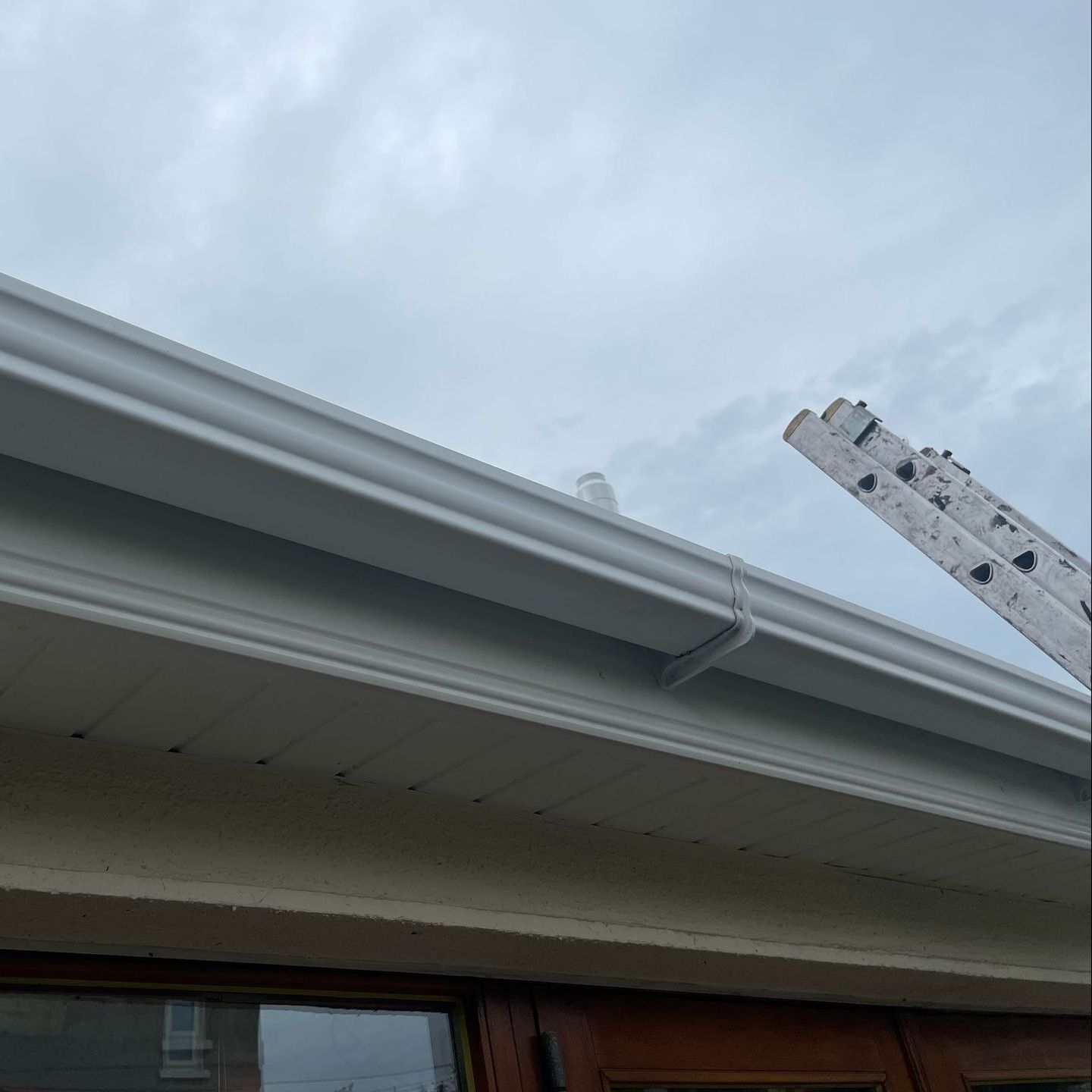A ladder is sitting on top of a white gutter on a roof.
