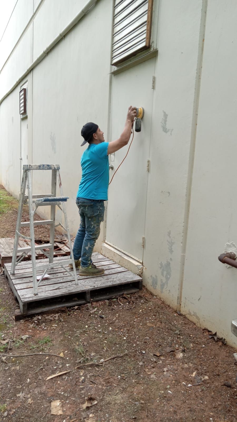 A woman is standing on a wooden pallet next to a building.