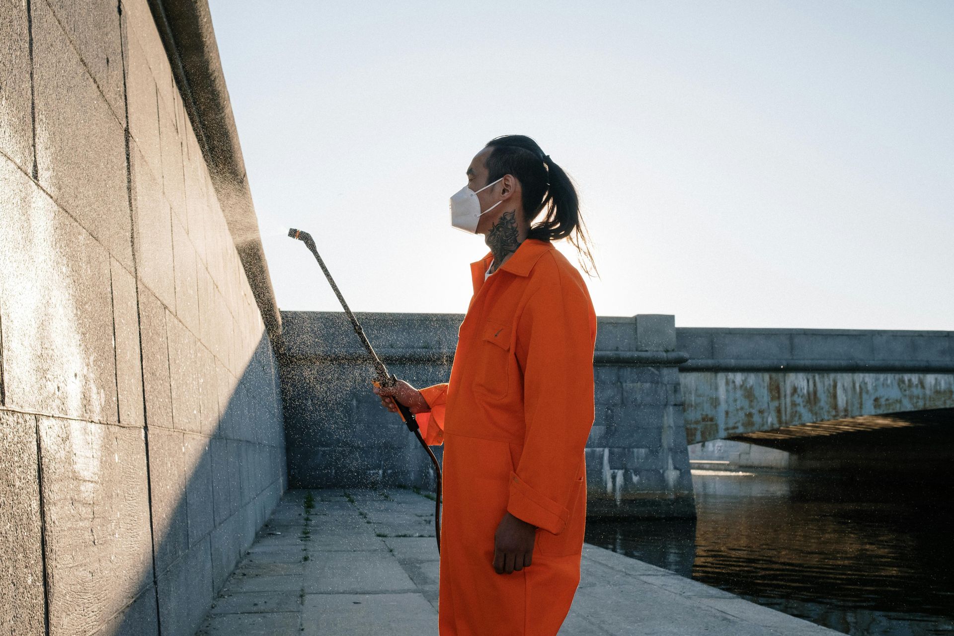 A man in an orange jumpsuit is spraying a wall with a sprayer.