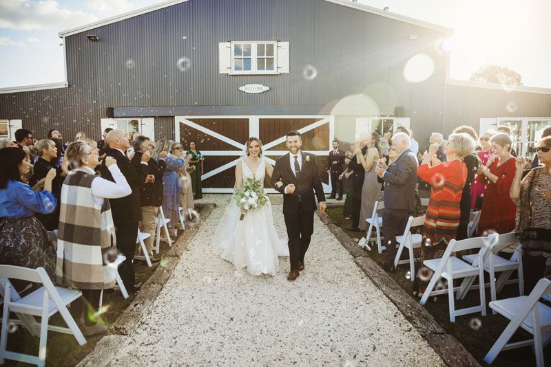 A bride and groom are walking down the towards the camera in front of Aberfeldy Barn.