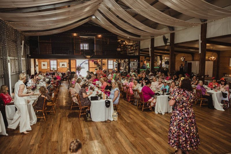 A woman is standing in front of a large group of people sitting at tables in Aberfeldy Barn.