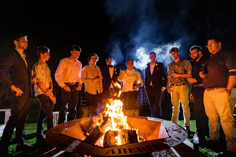 A group of men are standing around a fire pit at night at Aberfeldy Barn