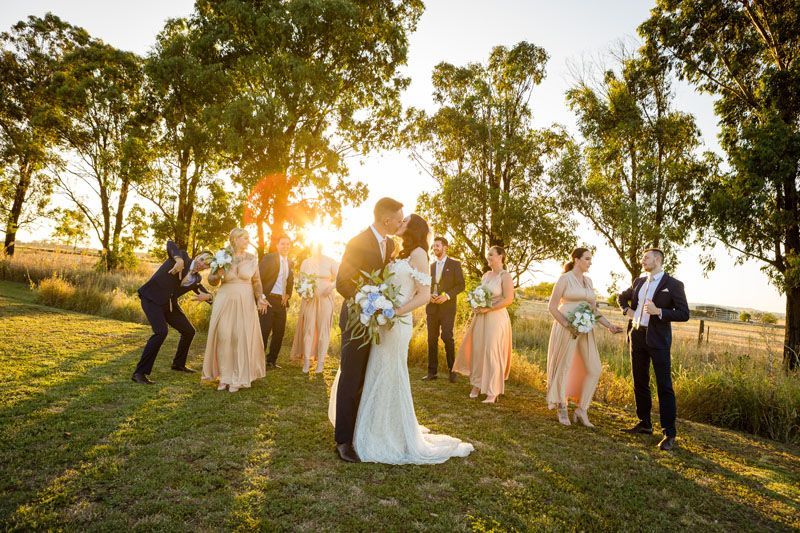 A bride and groom are kissing in front of their wedding party.