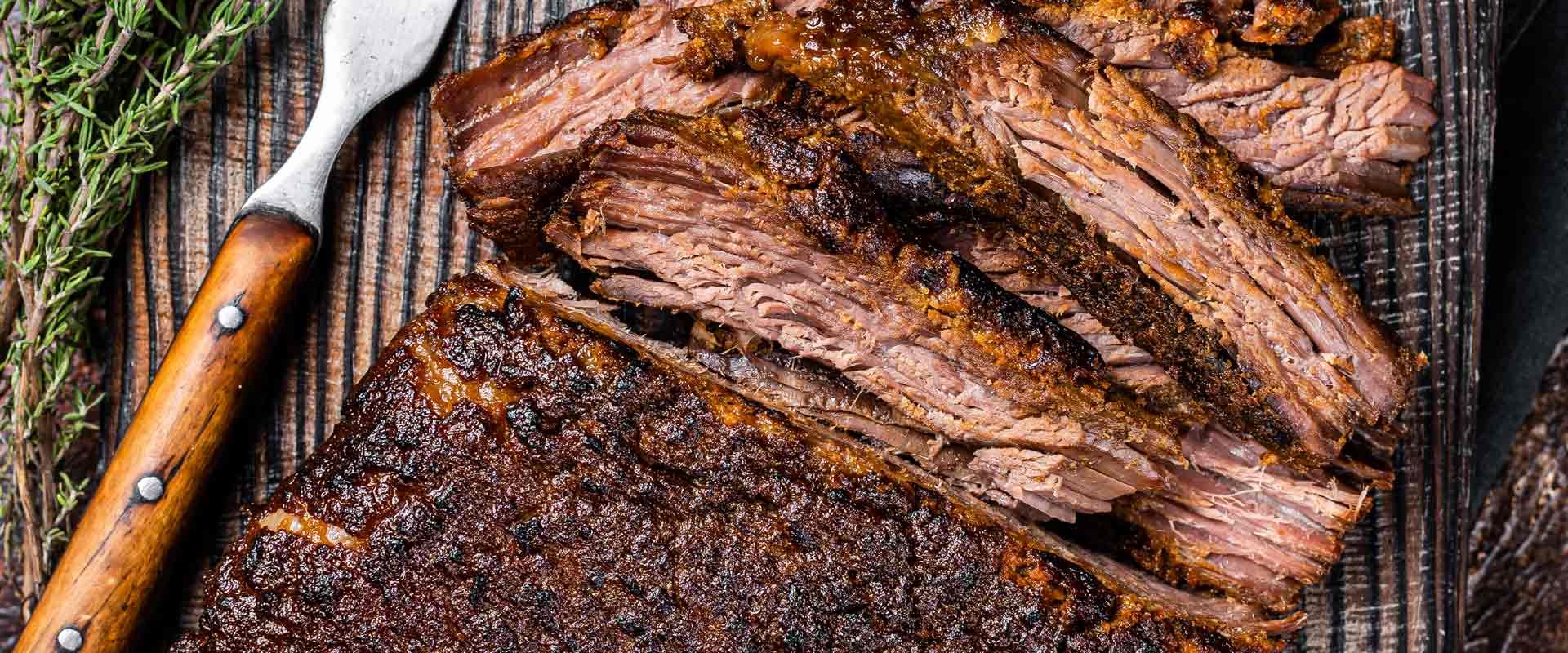 Sliced smoked brisket on a cutting board with a wooden-handled knife and striped cloth