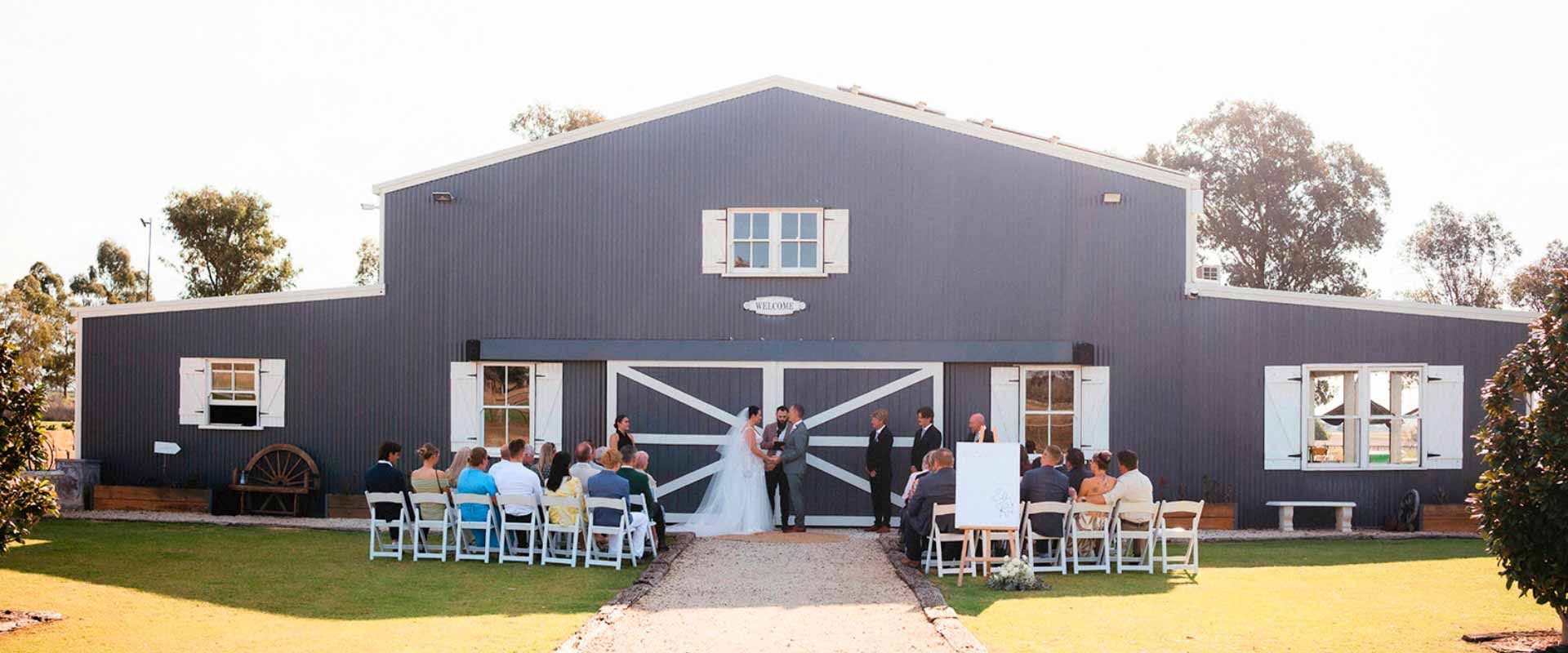 Wedding ceremony outside a Aberfeldy Barn; couple in front of barn doors. Guests seated on chairs.