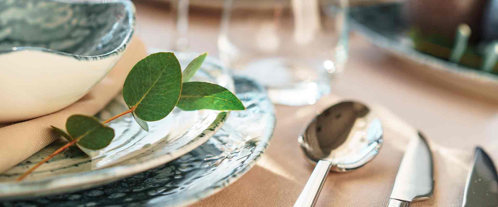 Elegant table setting with patterned plates, silverware, and a green leafy sprig beside a bowl of soup