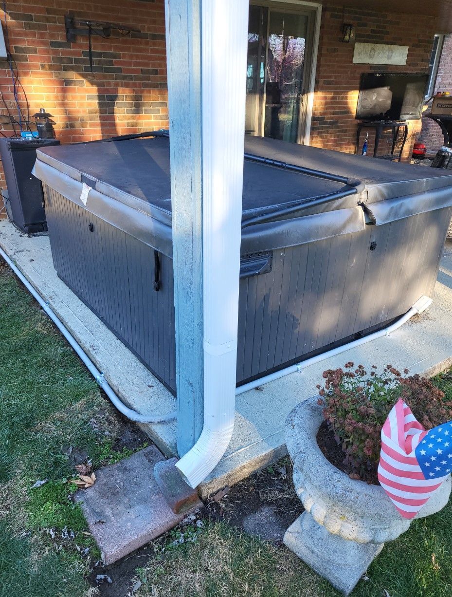 A hot tub is sitting under a porch next to a brick house.