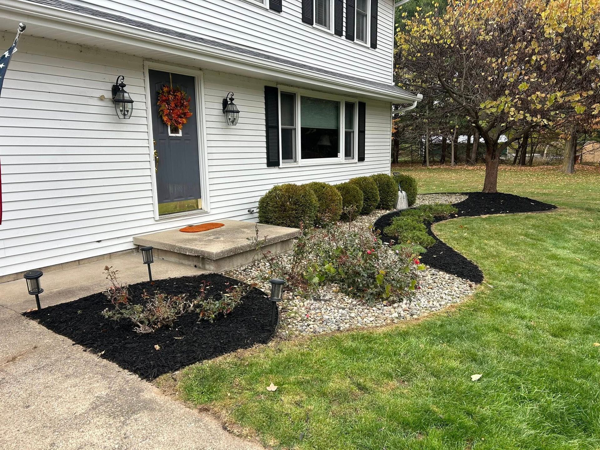 Front exterior of a white house with a gray door, landscaped garden beds featuring black mulch and green shrubs.