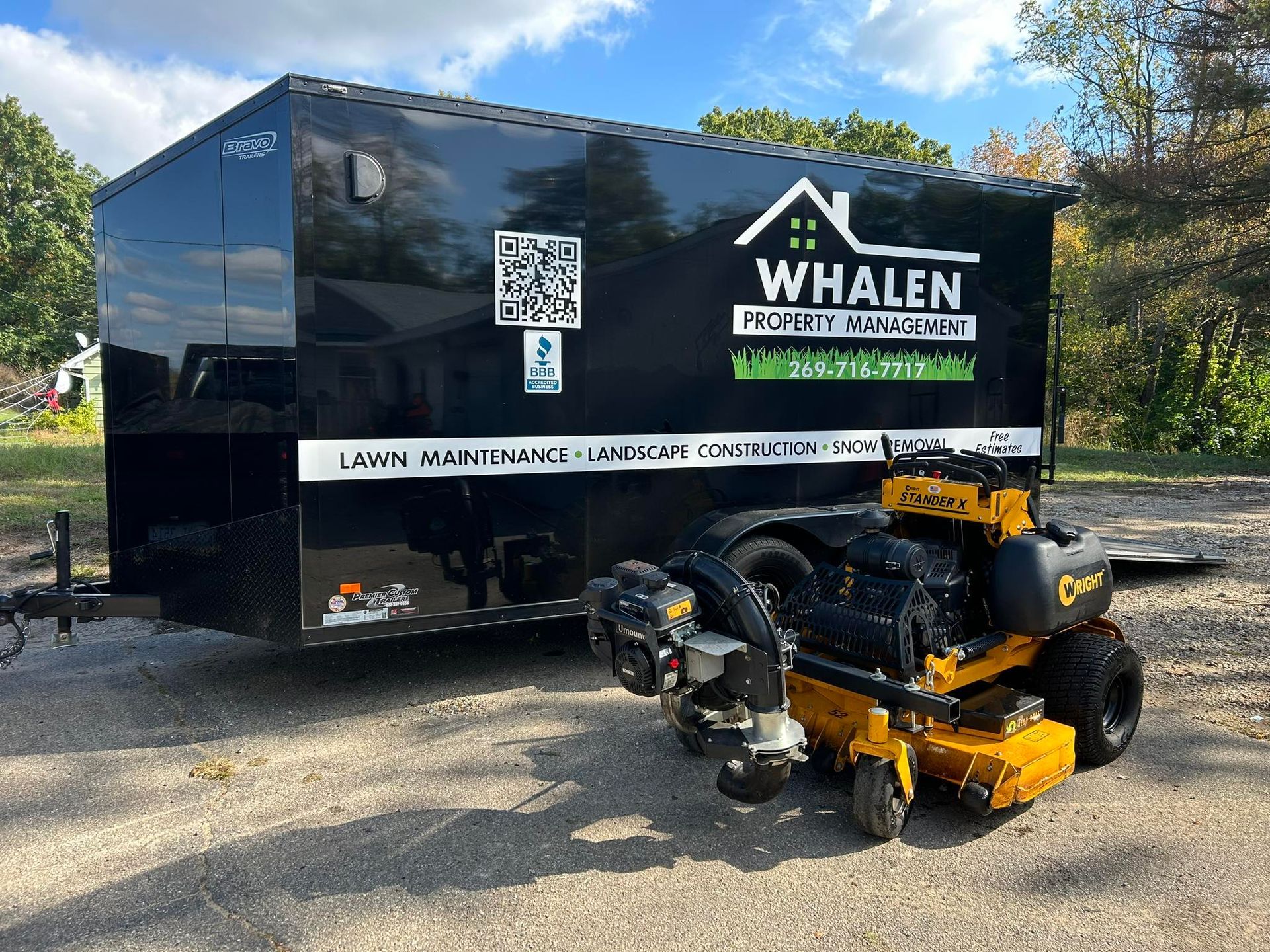 A black utility trailer for Whalen Property Management parked outdoors with a yellow riding lawn mower parked in front.