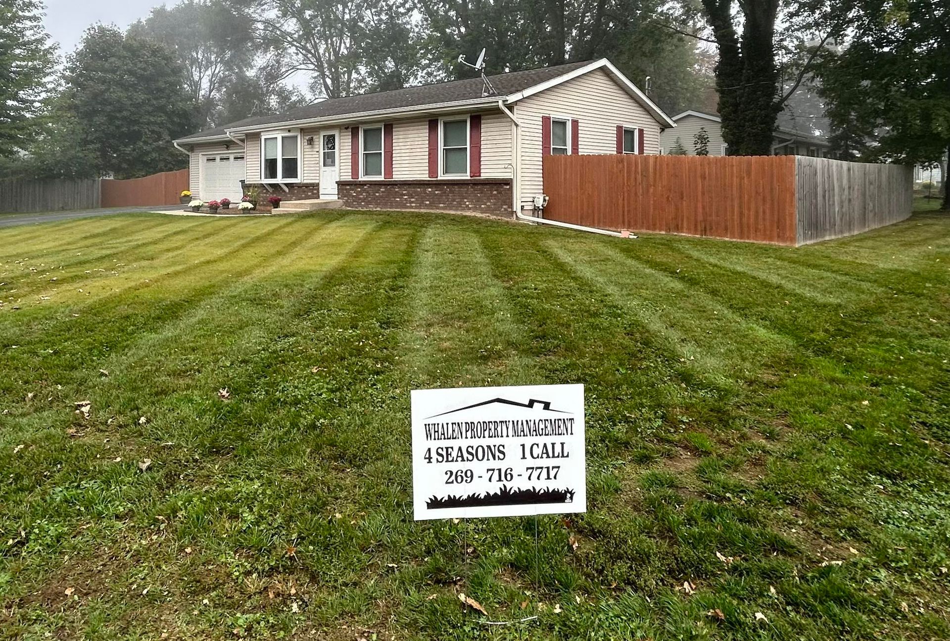 A freshly mowed residential lawn with a lawn care advertisement sign in the foreground, in front of a beige house.