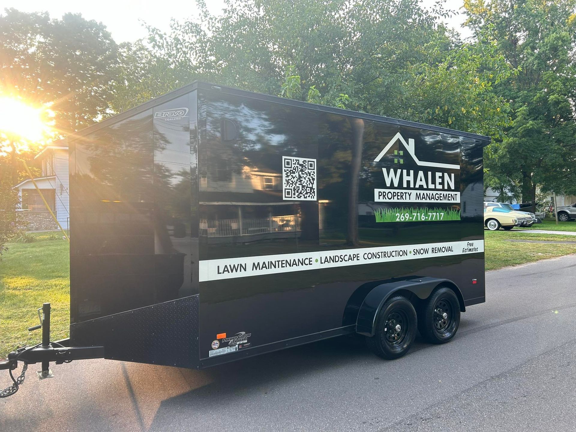 A black trailer parked on a street displays the white Whalen Property Maintenance logo, a QR code, and service text.