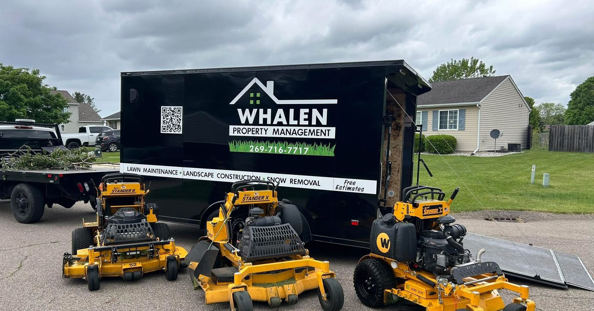 Three yellow commercial zero-turn lawn mowers parked in front of a black Whalen Property Maintenance cargo trailer.