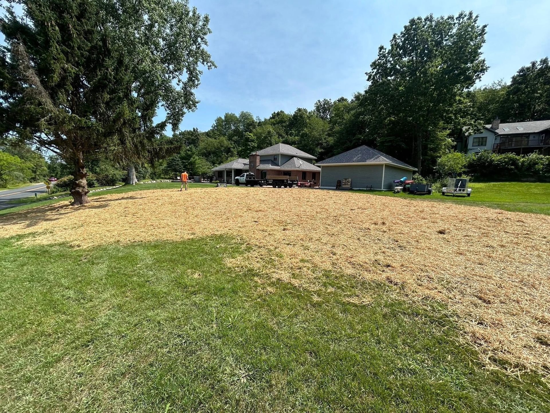 A large area of freshly mulched dirt in a residential lawn, with houses and trees in the background under a blue sky.