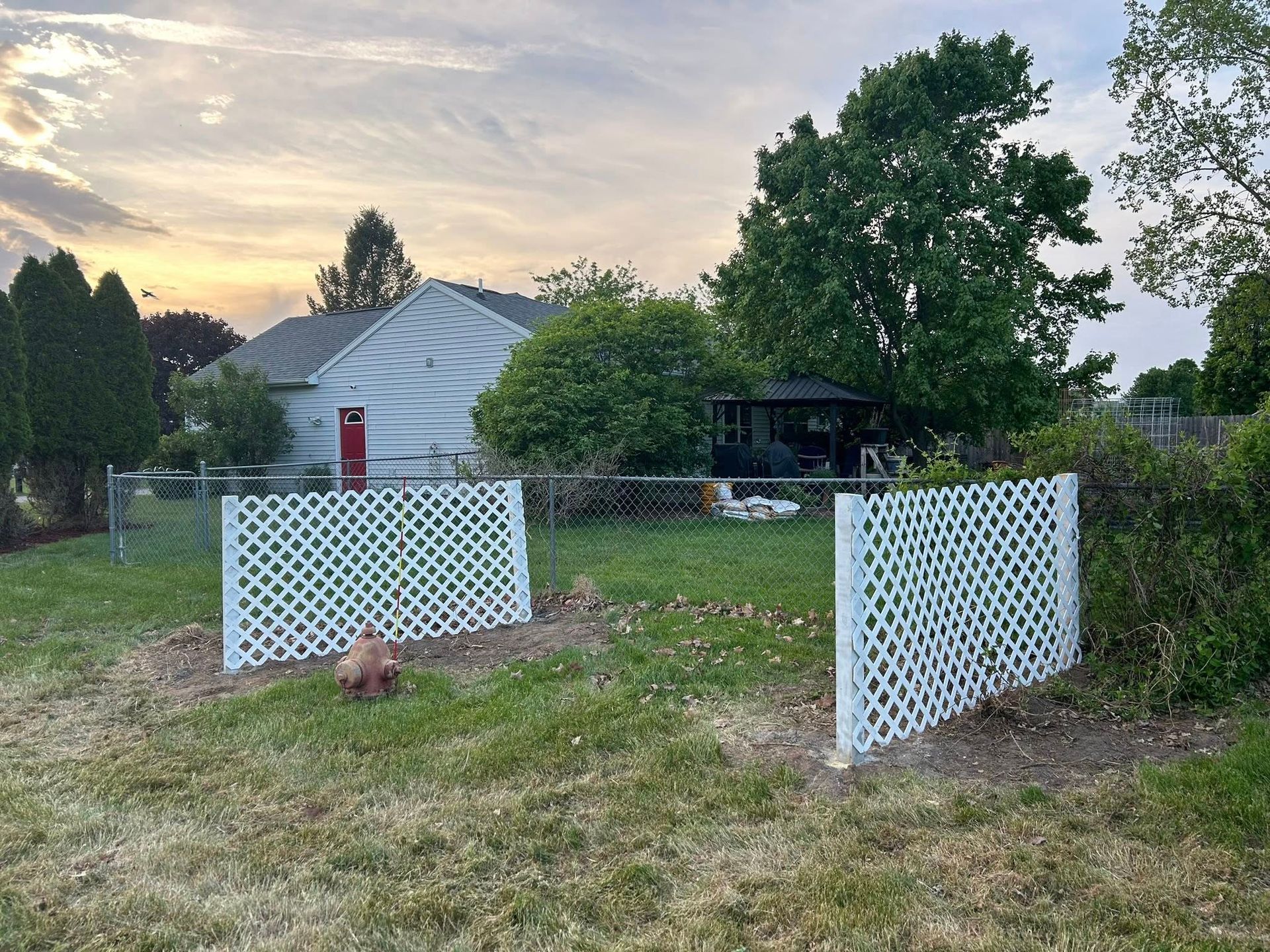 Two white lattice garden panels stand in a grassy backyard under a sunset sky.