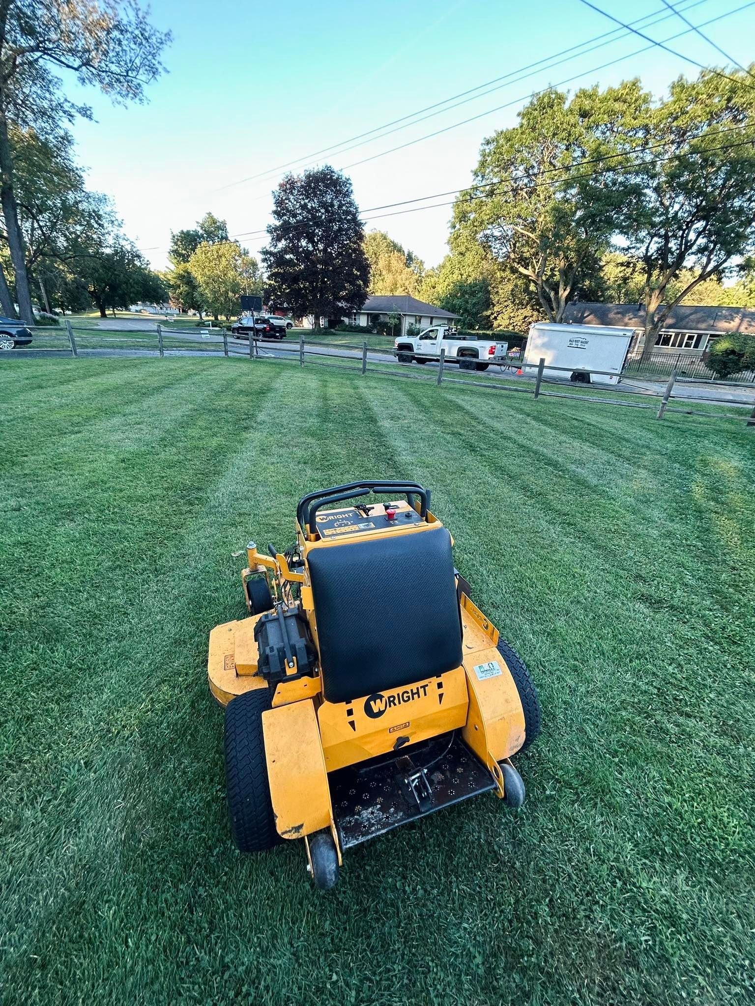 A bright yellow zero-turn lawn mower sits in the middle of a freshly mowed grassy yard on a sunny day.