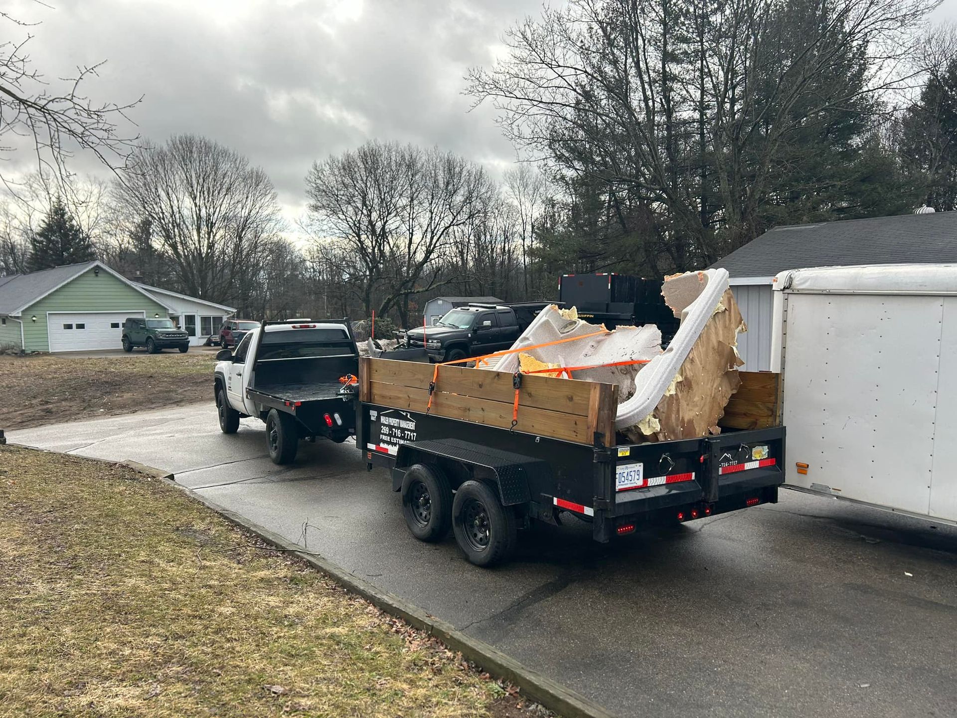 A black pickup truck pulling a trailer filled with debris and large furniture, parked on a driveway in a residential area.