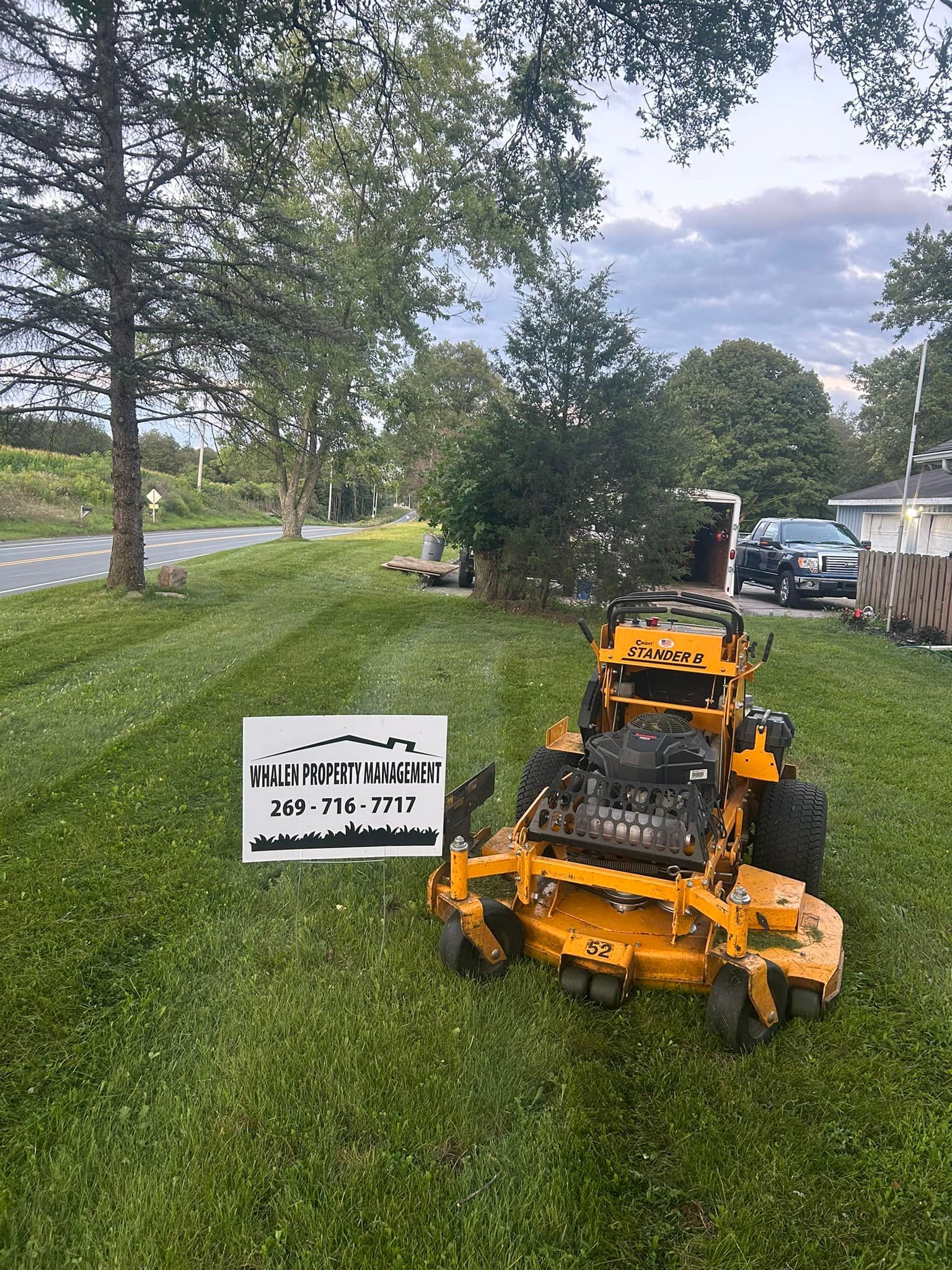 A yellow Scag zero-turn mower sits on a freshly mowed lawn next to a sign for 